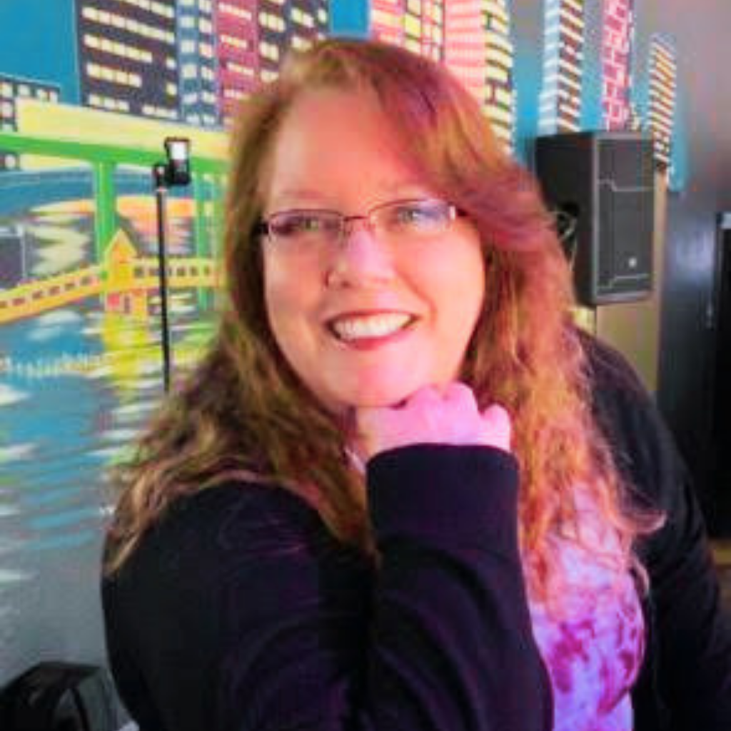 Smiling woman with glasses and a pink scarf posing indoors against a colorful city mural backdrop.